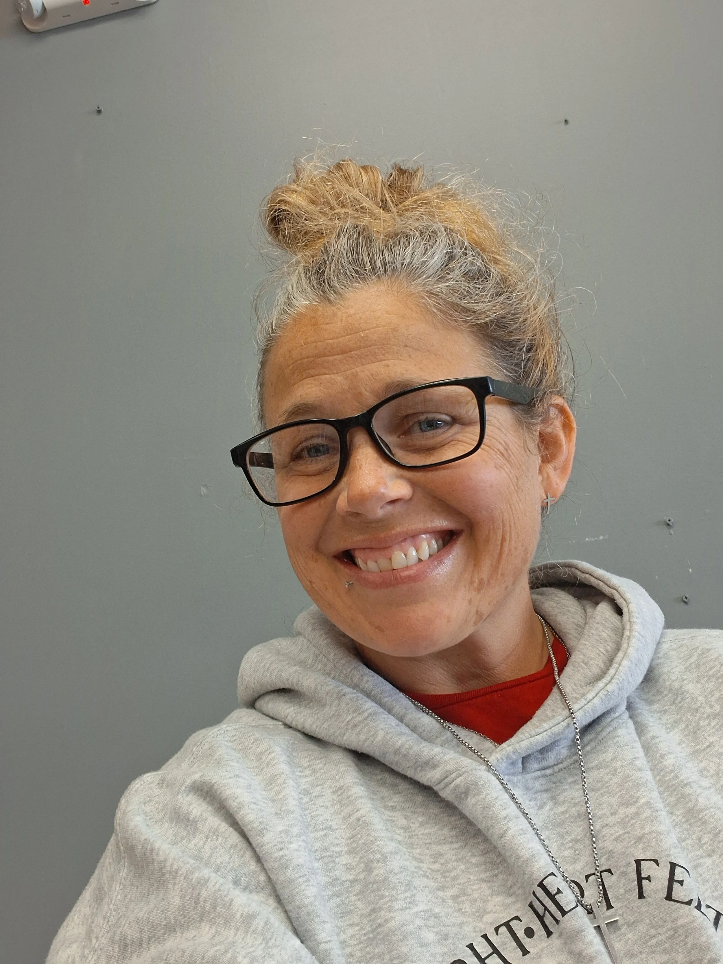 Image of Caucasian woman with curly brown hair wearing glasses and a gray sweatshirt