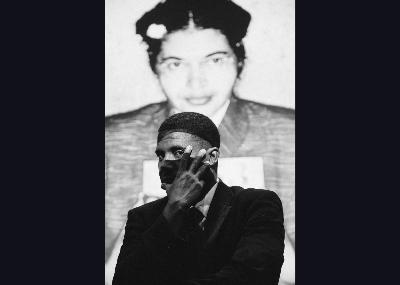 Image of a man with his hand on his face standing in front of a photograph of Rosa Parks.