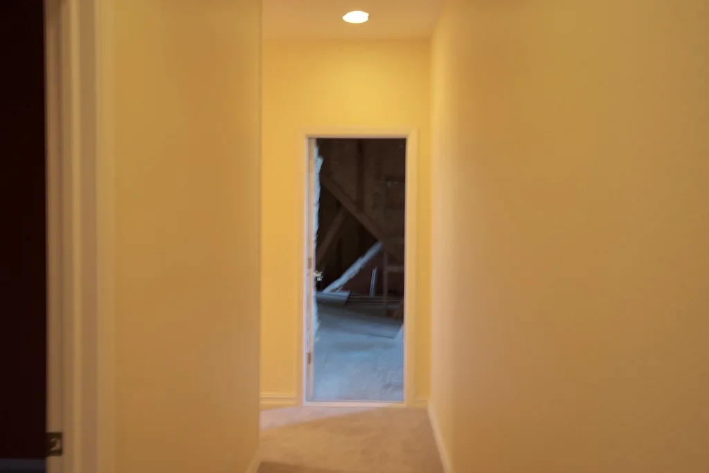 Sorry for the blur. This is from just past the middle of our upstairs hall, looking toward the east. On the left is a door into a bedroom, which will be a casualty of our renovation. We'll be talking out about the eastern half of the room to open up that end of the hallway. The remaining half will be the new linen and storage closet. We'll also add a skylight. Directly ahead is the open door into the attic space over the east end of the house. If you turn the corner and go left, instead of into the attic, there is a linen closet—another casualty— right next to the attic doorway. Then, after the linen closet, there is the back stairway that leads down into the laundry room.