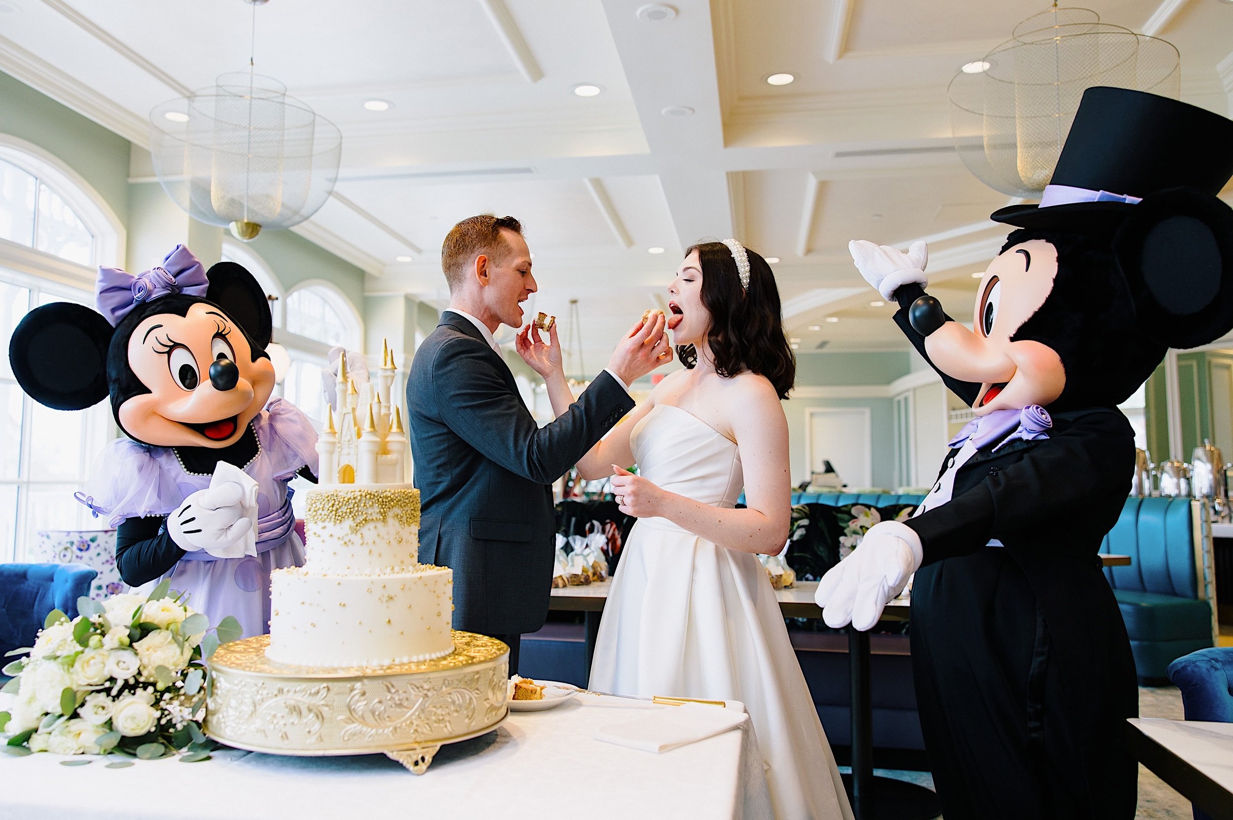116-ZacWolfPhotography-20221122-Blog_Bride-and-Groom-eating-wedding-cake-with-Mickey-Mouse-and-Minnie-Mouse.jpg
