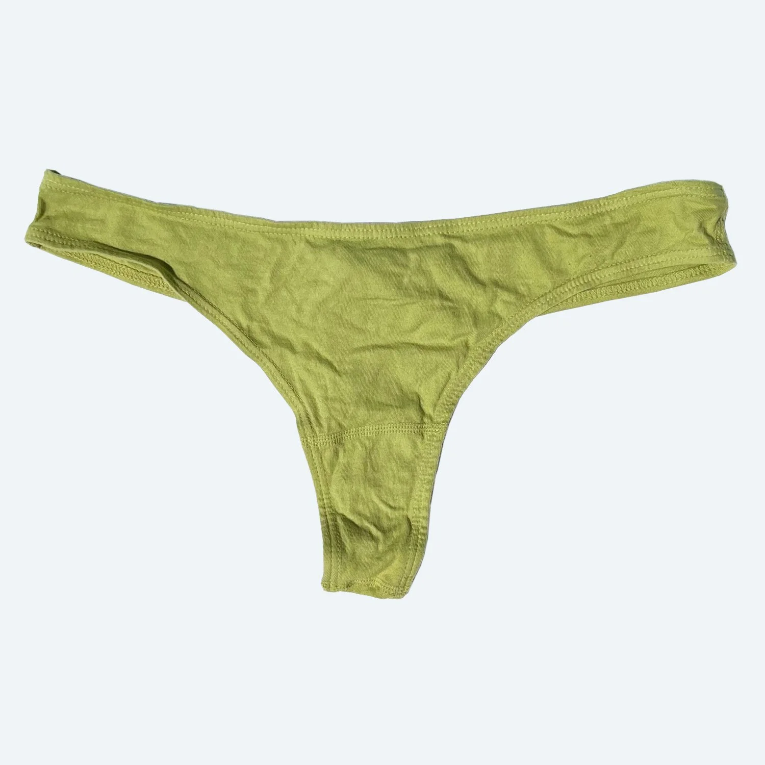 Flat lay of Pansy thong in avocado green on a pale blue-gray background.