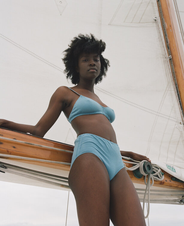 a woman wears "Siren"-colored Pansy bra and high-rise underwear while standing on a boat against the backdrop of a sail