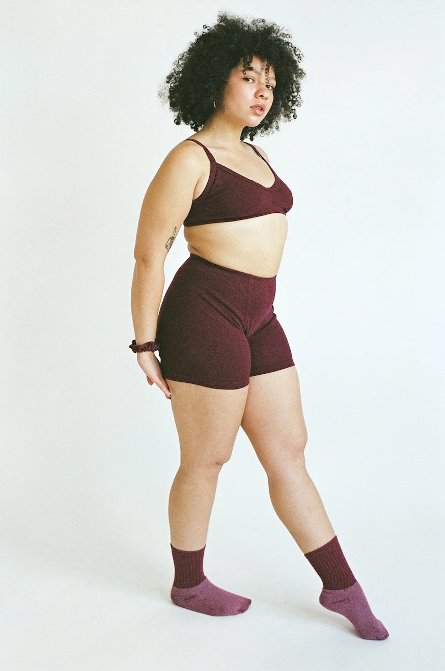 A model wear's Pansy Stretch Shorts in the color Wine with a matching bra, socks, and scrunchie.