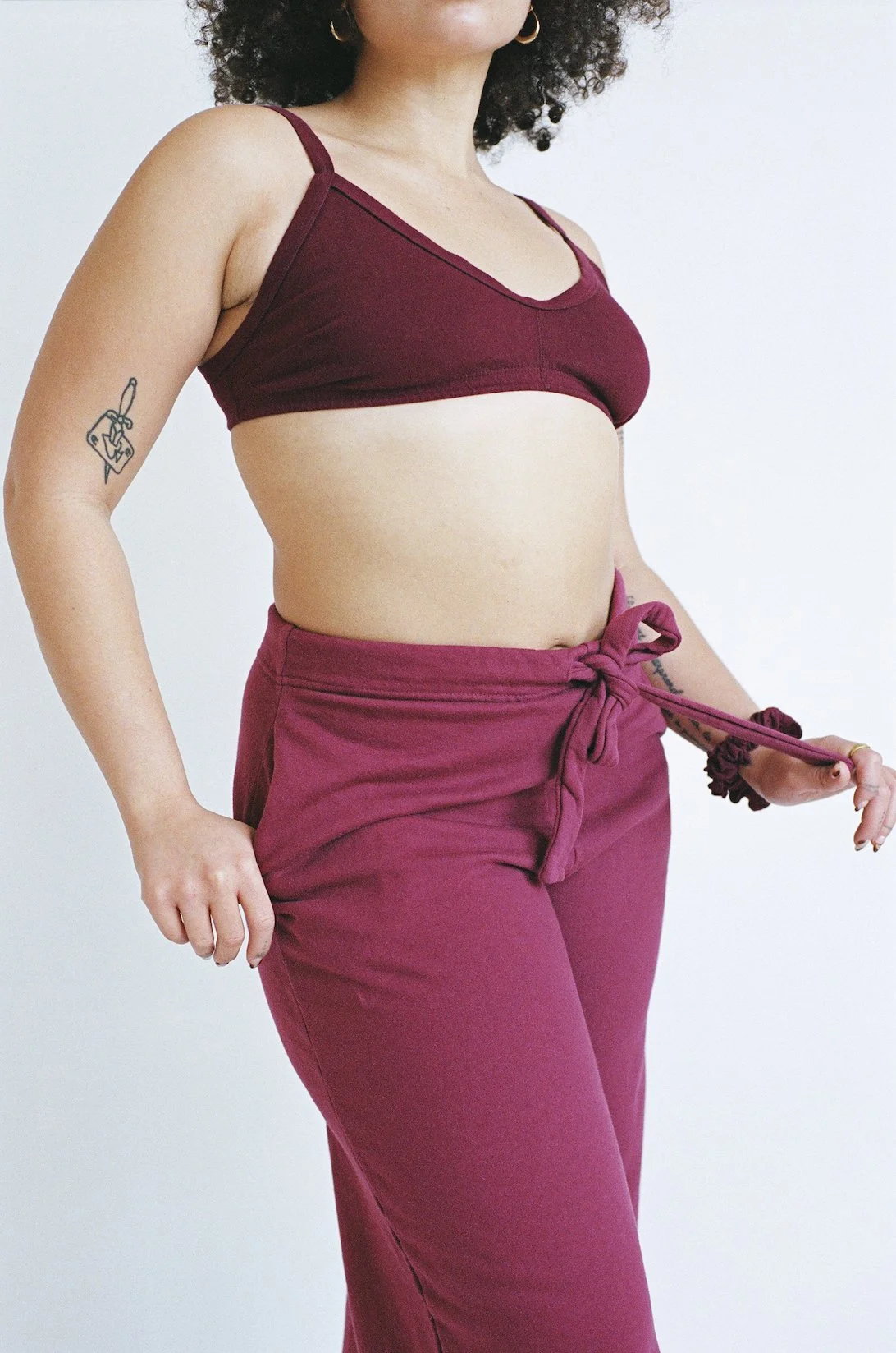 A model wearing Wine-colored Pansy Fleece Pants tugs at her drawstring and rests her hand in the pocket of her pants.
