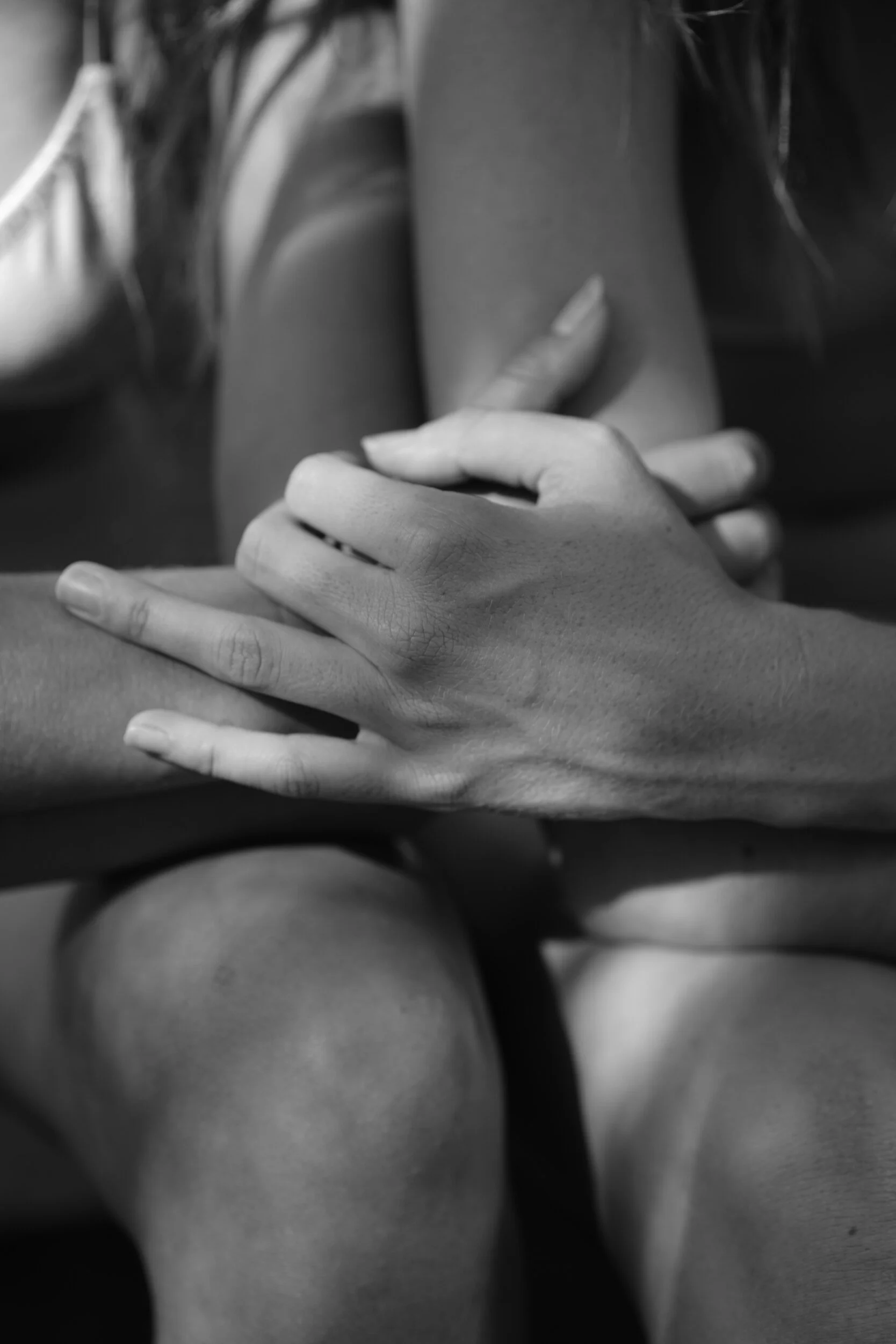 A black-and-white close view of two seated models holding one another’s arms.