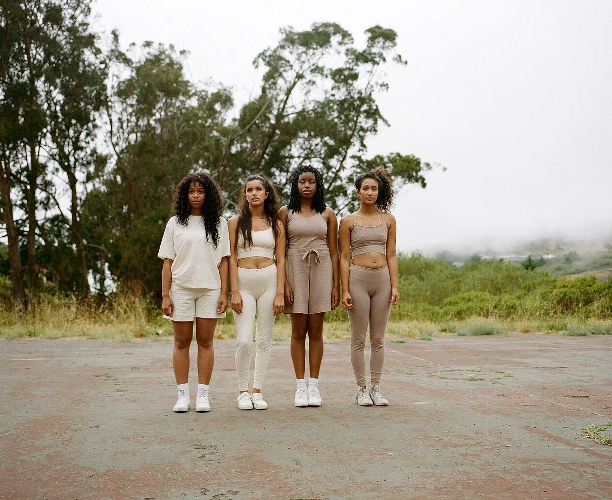 Four models in cream and mauve sportswear stand shoulder to shoulder on the court.