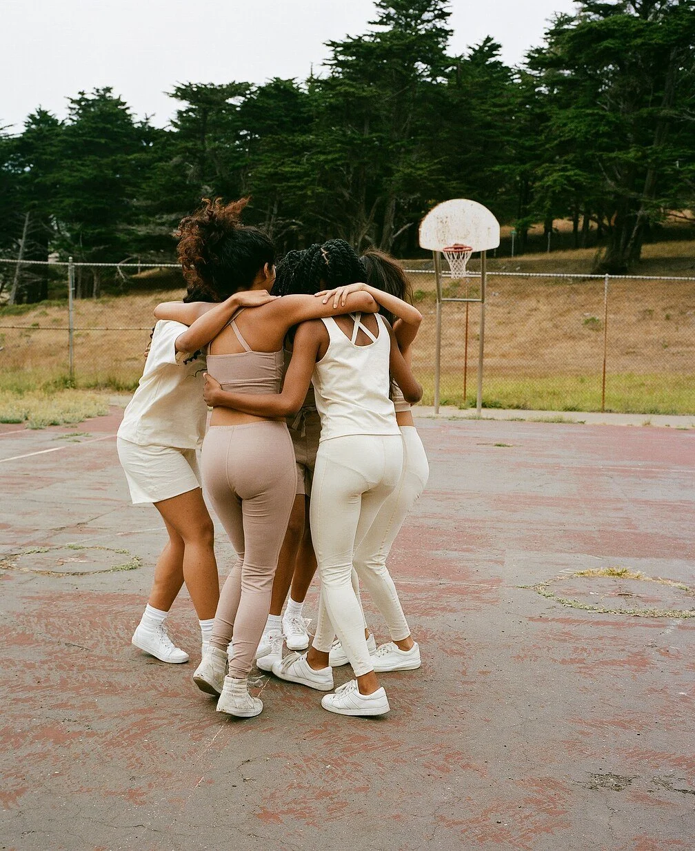 A group of models in cream and mauve sportswear huddles with their arms around one another on the court.