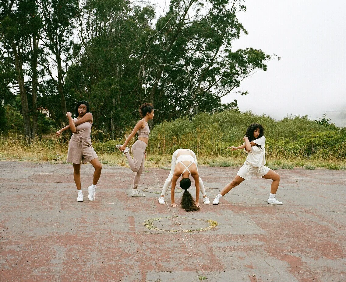 Four models stretch on the court, bending forward, lunging, balancing on one leg and stretching an arm.