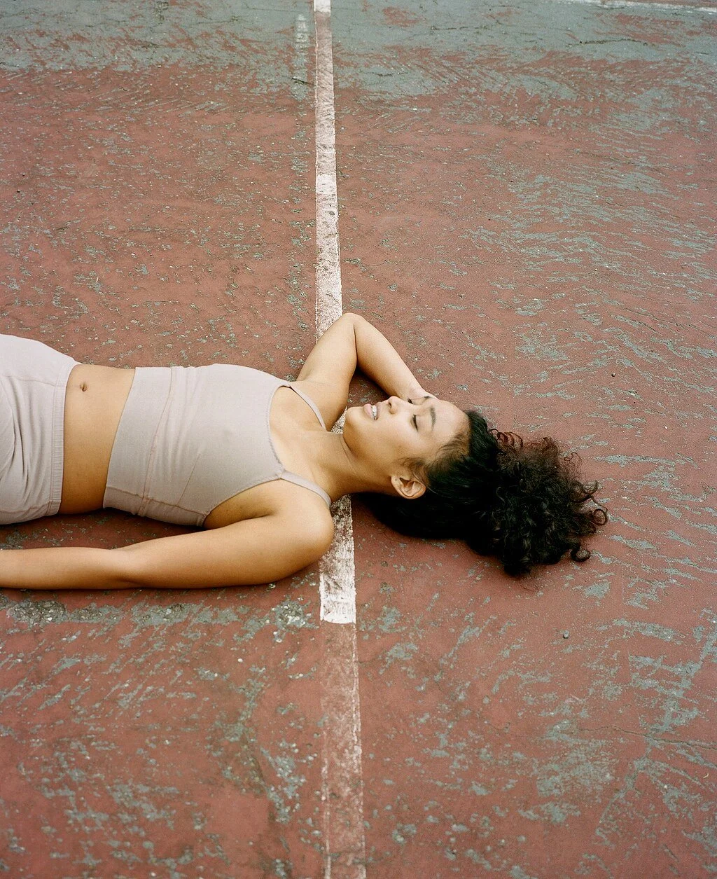 A model in a mauve crop top lies on the court with one hand behind their head and eyes closed.