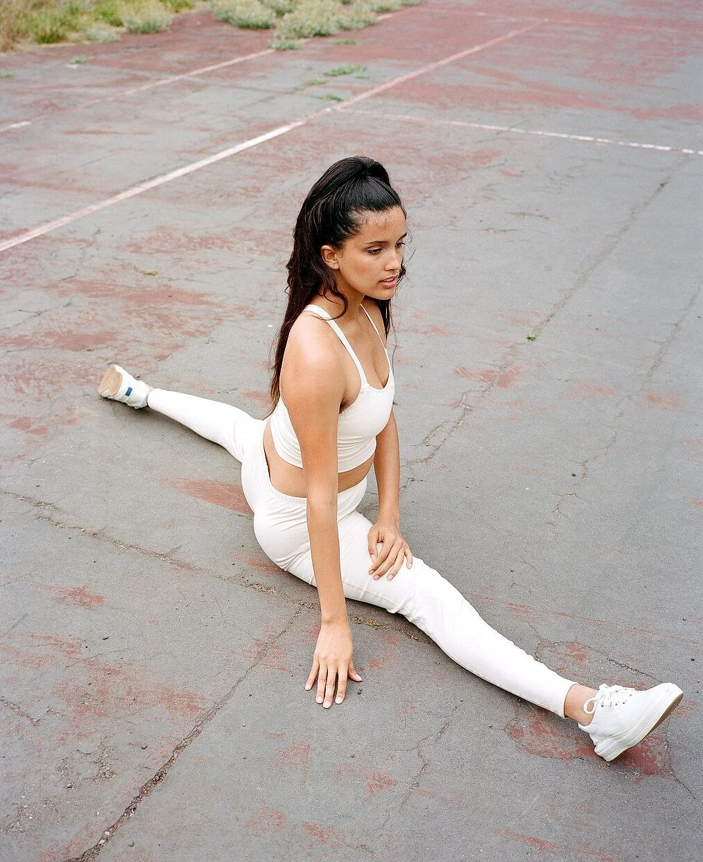 A model in a cream crop top and leggings does the splits on the court in white sneakers.