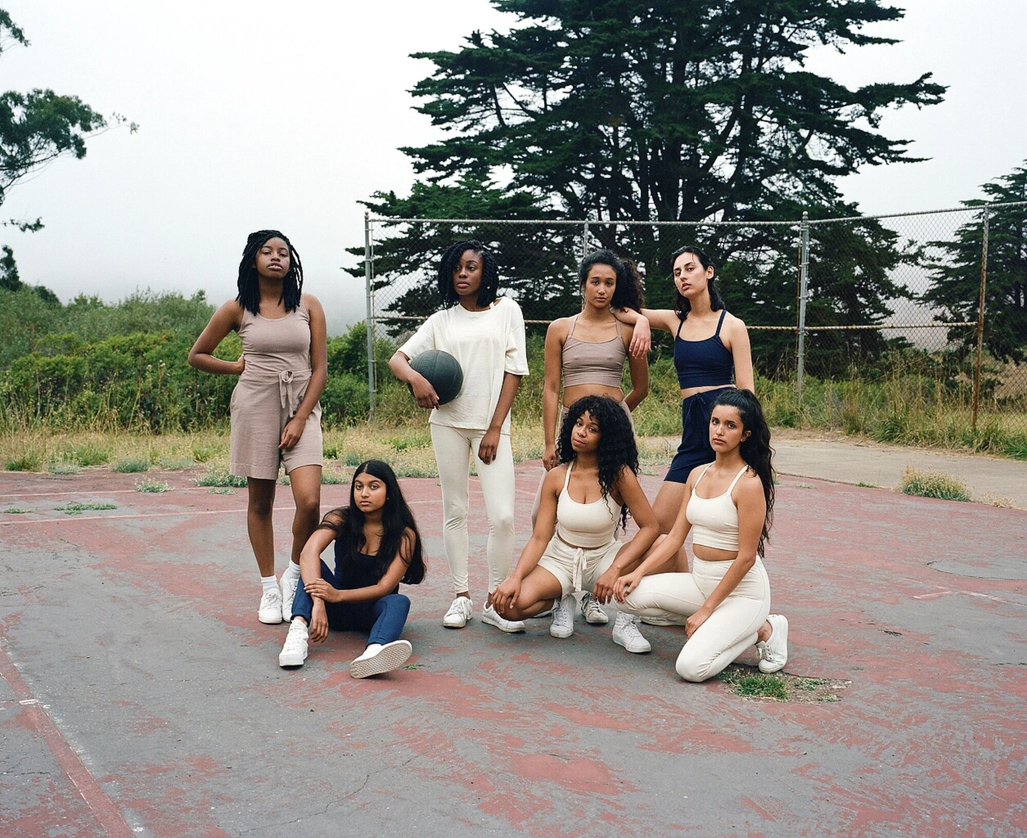 Seven models in navy, cream and mauve sportswear pose together on the court, standing, sitting and kneeling.