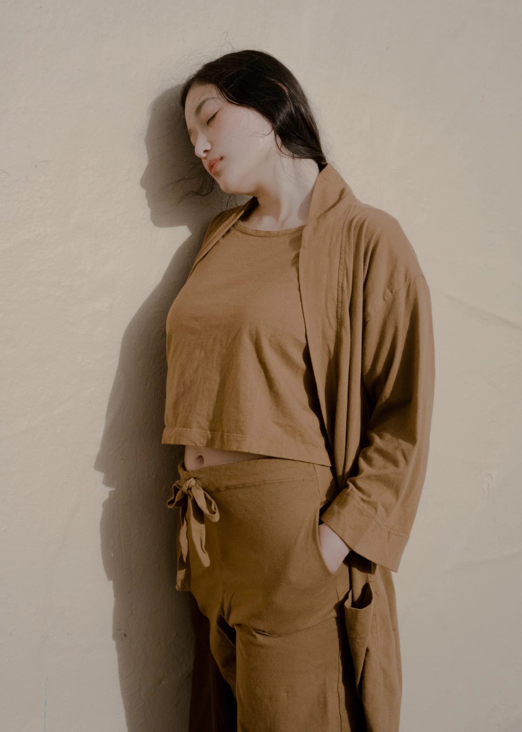 Front view of a model wearing the Pansy organic cotton Crop Top in Almond brown with matching pants and an open robe.