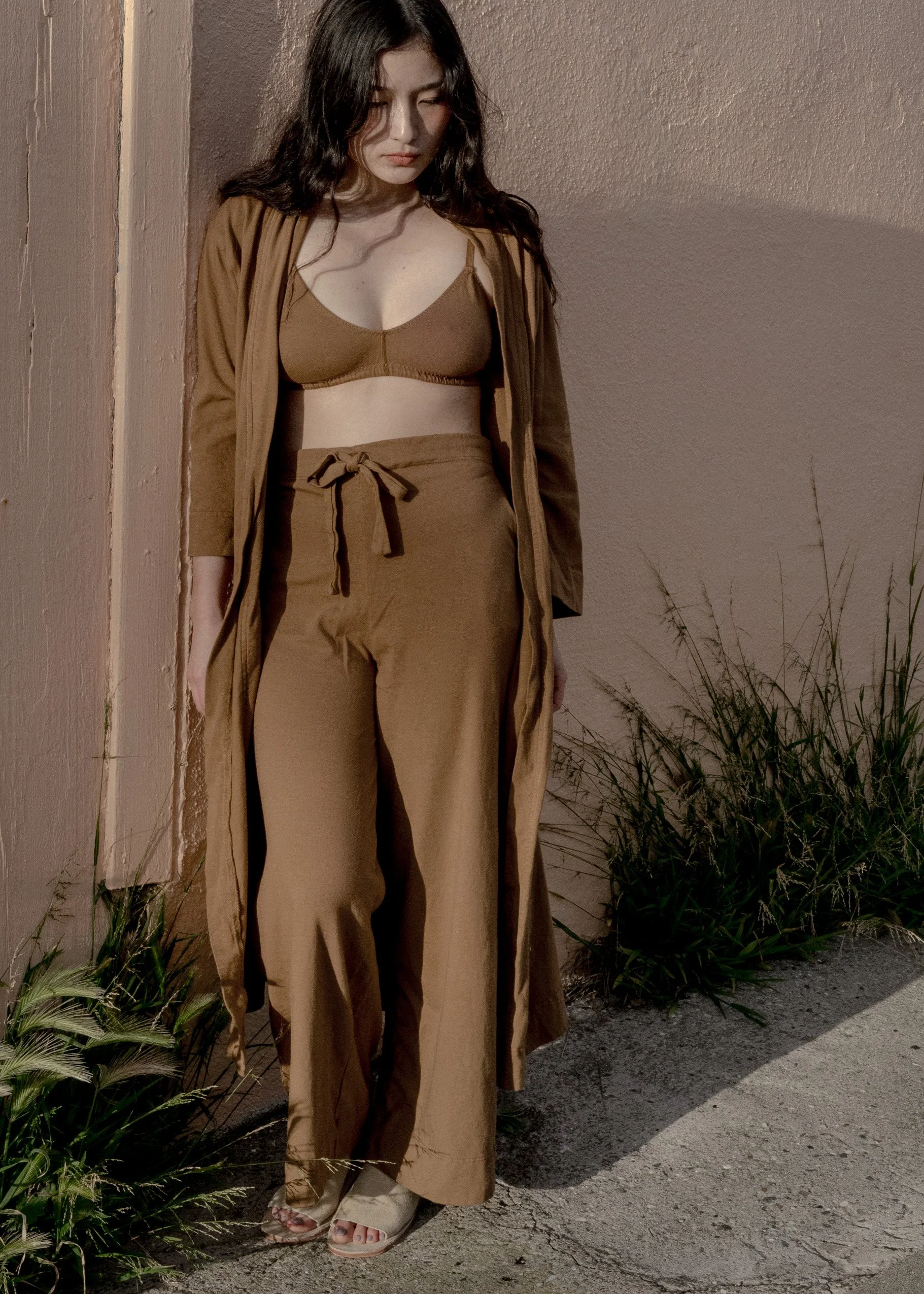 Front view of a model wearing Pansy organic cotton Drawstring Pants in Almond with a matching bra and open robe.
