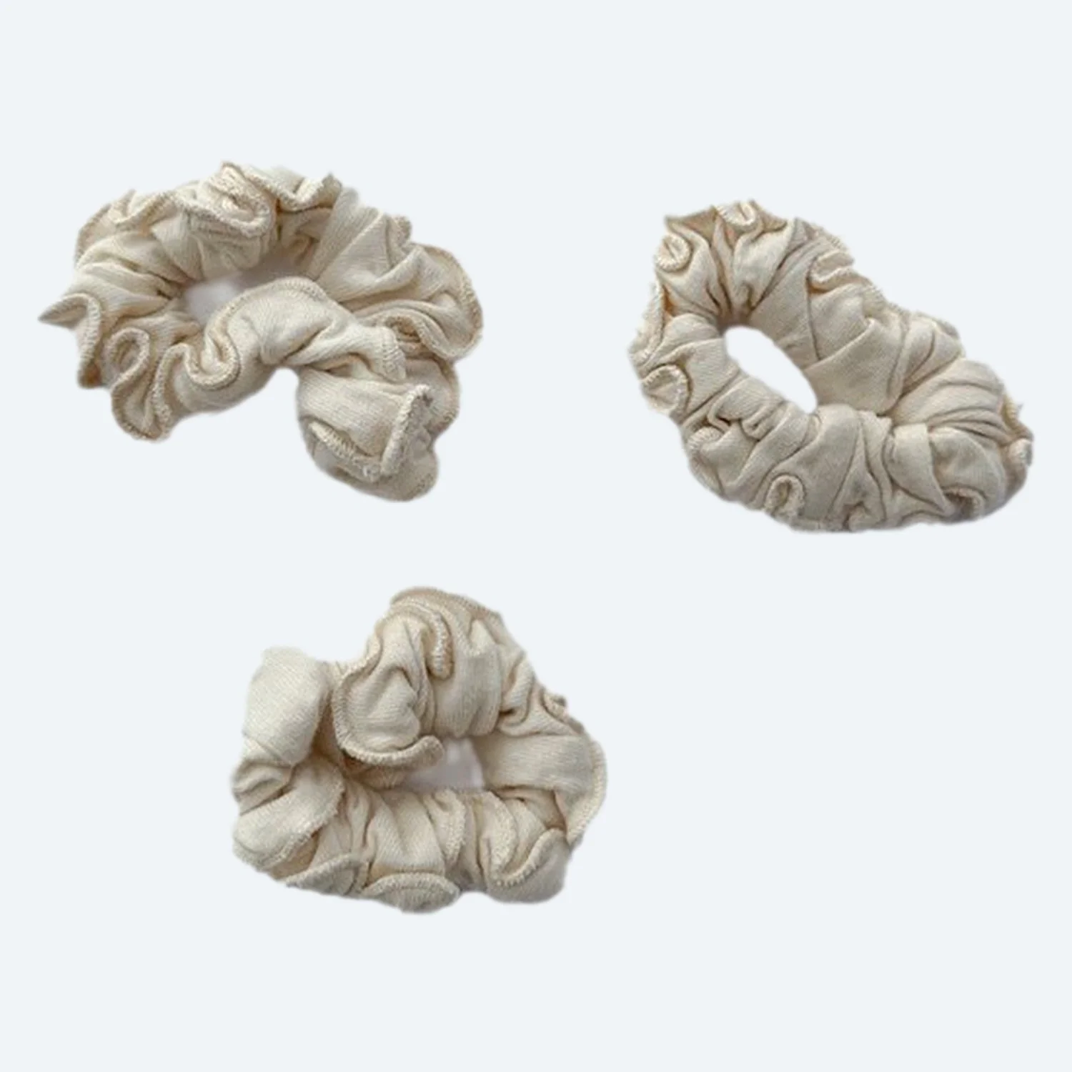 Three Pansy organic cotton scrunchies in Natural cream, laid flat.