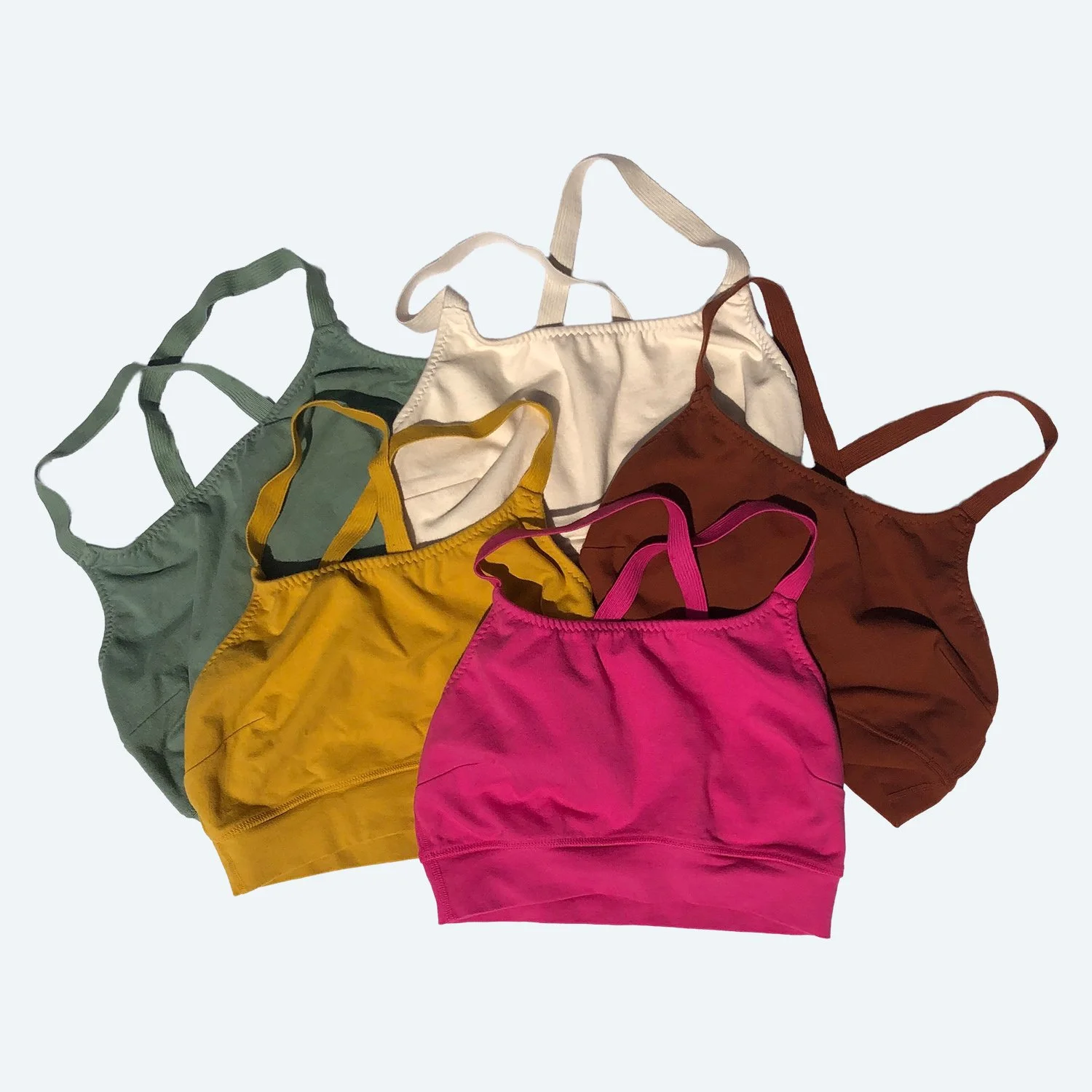 Flat lay of Pansy surprise sports bras in assorted colors on a pale blue-gray background.