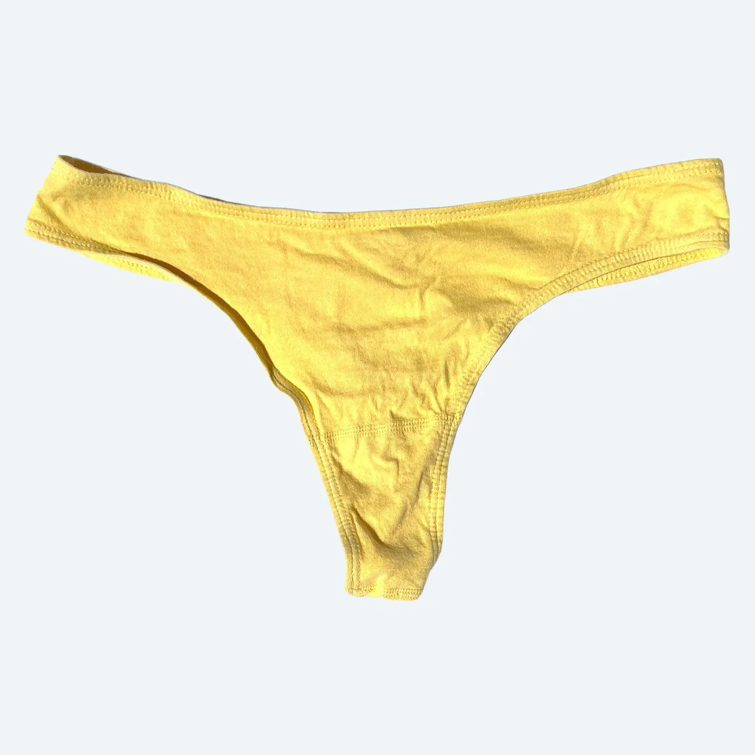 Flat lay of Pansy thong in butter yellow on a pale blue-gray background.
