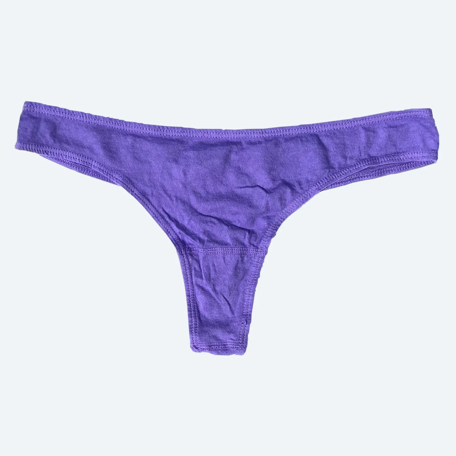 Flat lay of Pansy thong in lilac purple on a pale blue-gray background.
