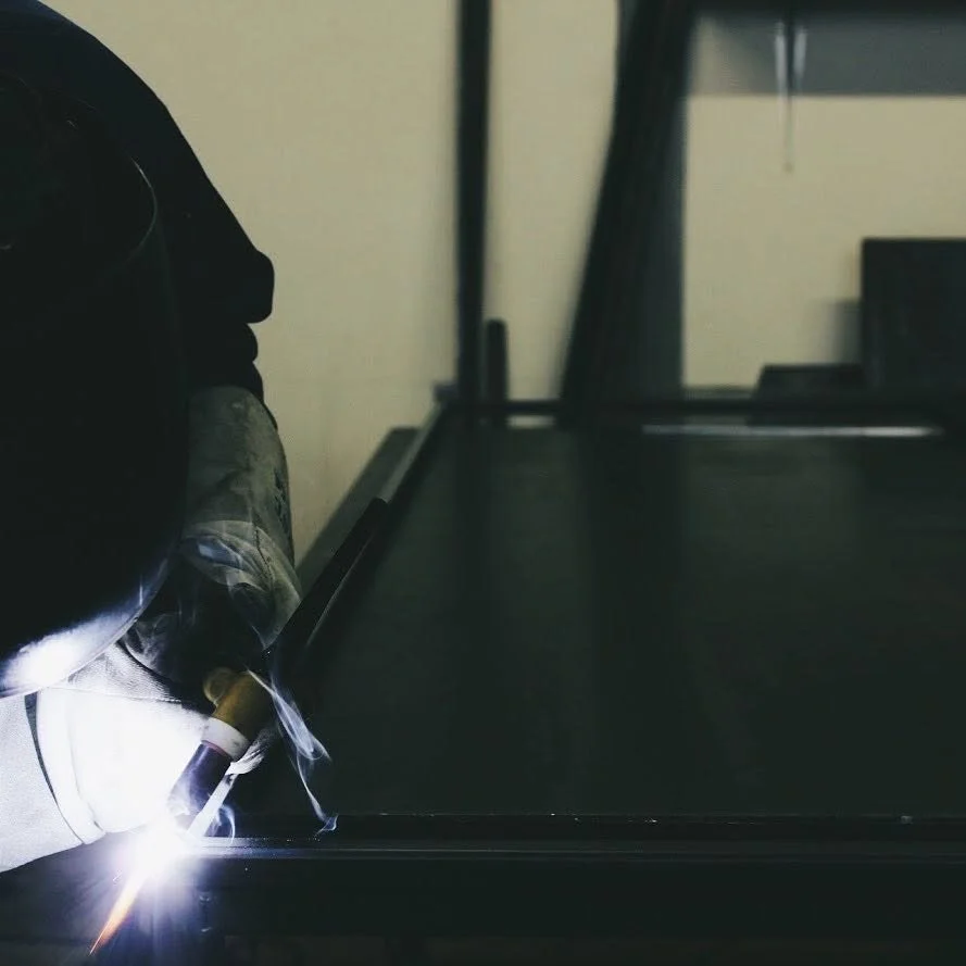 A person welding steel on a work table, with sparks and smoke.