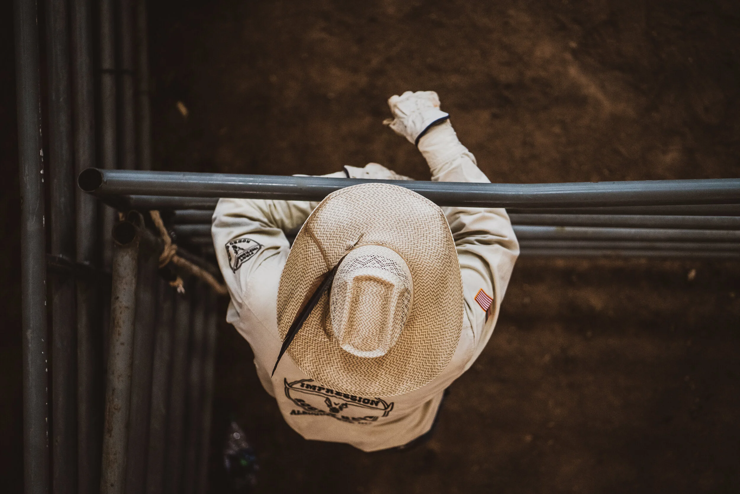 A person wearing a tan hat and a beige jacket with a flag patch on the sleeve, standing behind metal bars, viewed from above.
