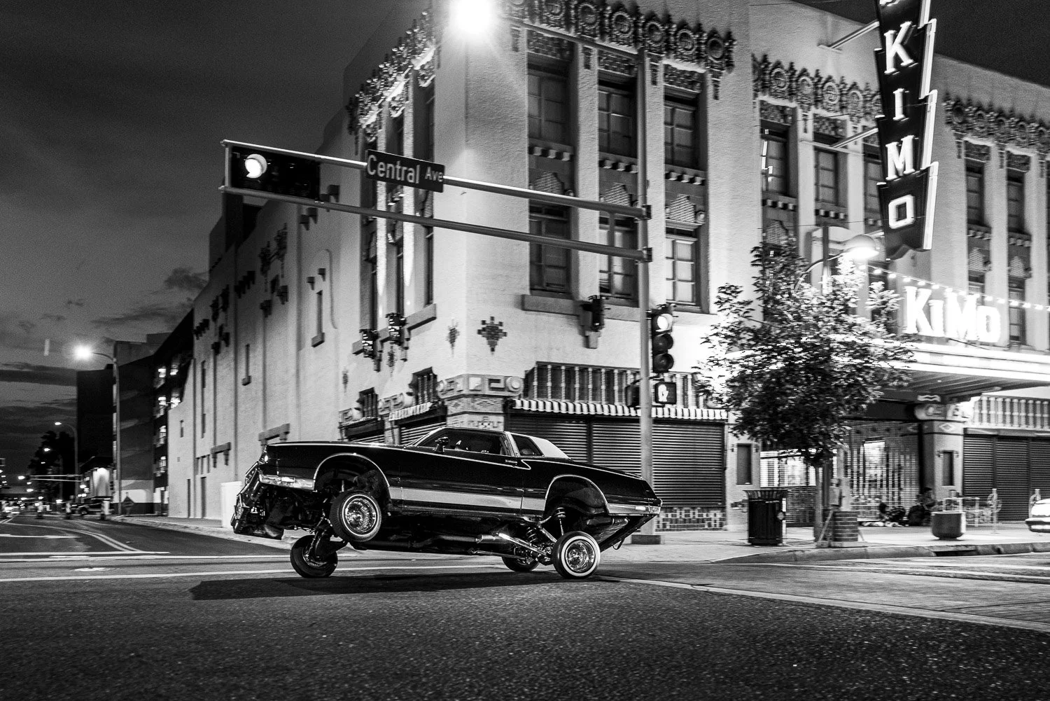 A lowrider up on 3 wheels at the Kimo Theater on Central in downtown Albuquerque at night.