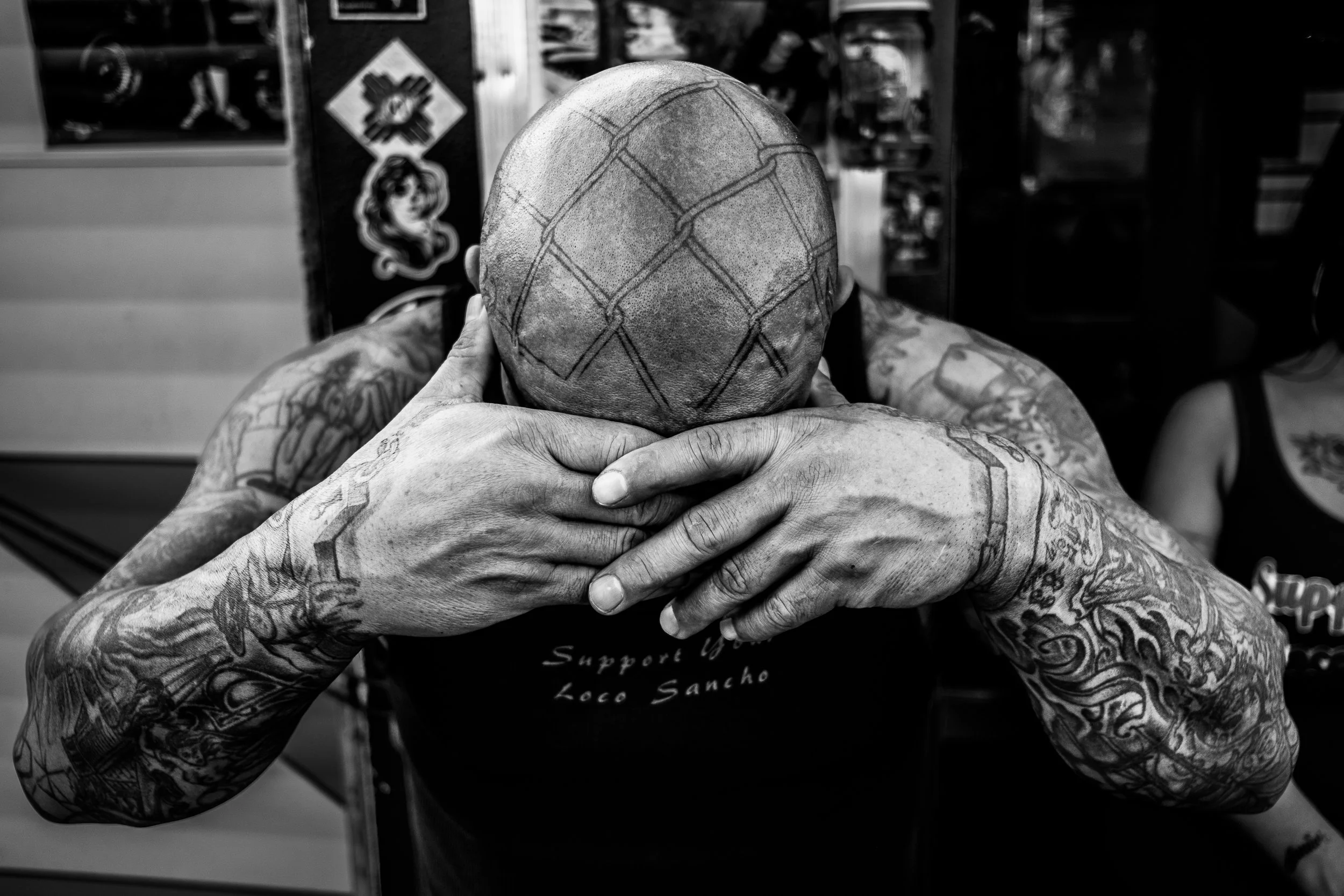 Black-and-white portrait in Albuquerque of a tattooed man with his head bowed and hands covering his face.