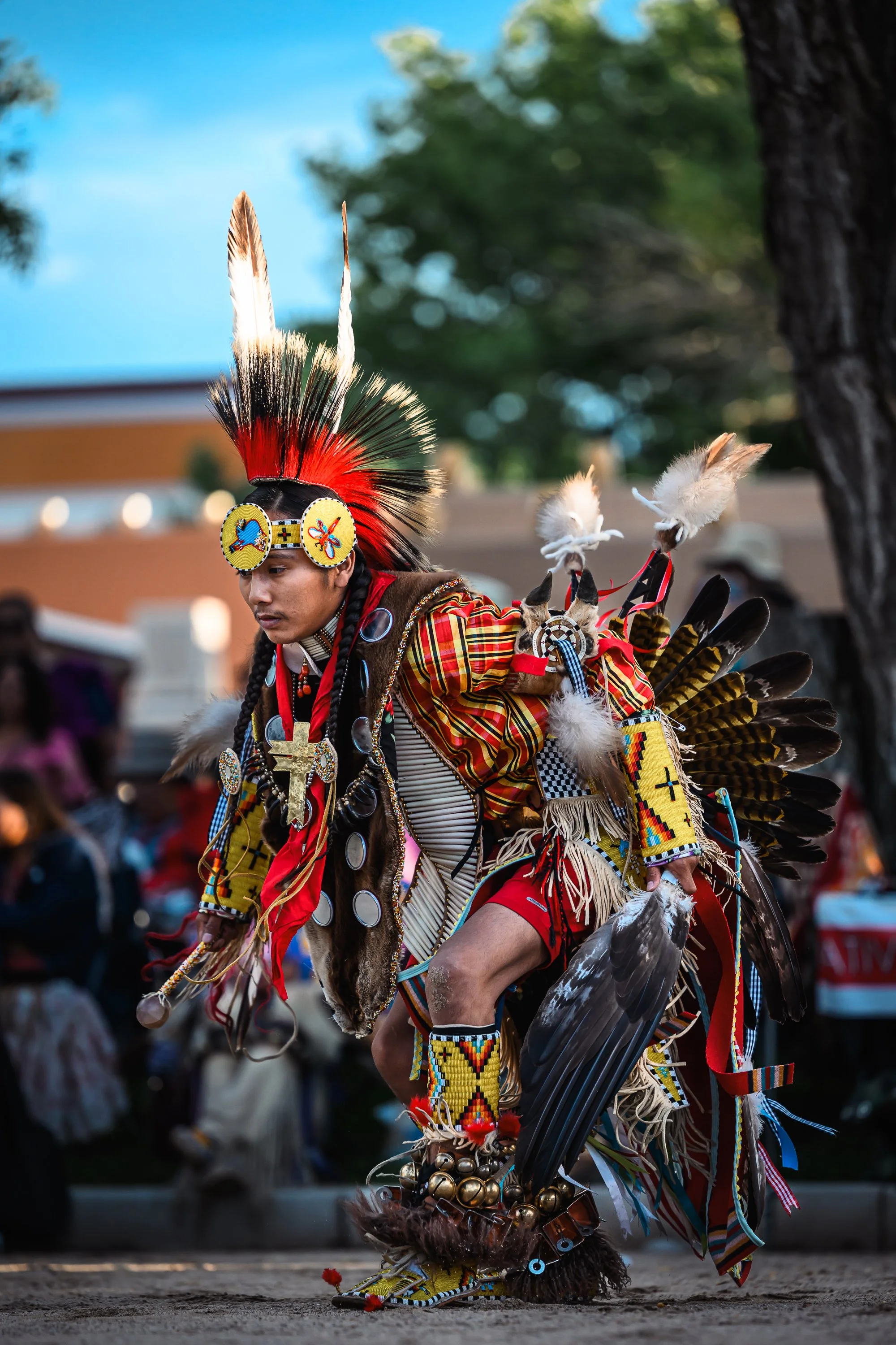 Native American man performing a traditional dance at a cultural event, dressed in elaborate colorful regalia with feathers, beadwork, and accessories.