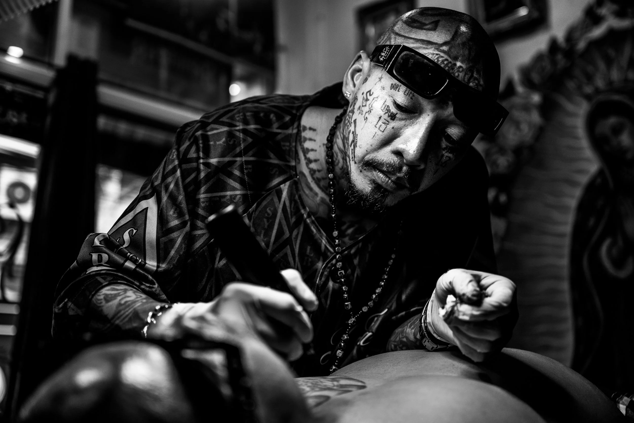 Man with tattoos and sunglasses on his head practicing tattooing on someone's skin.