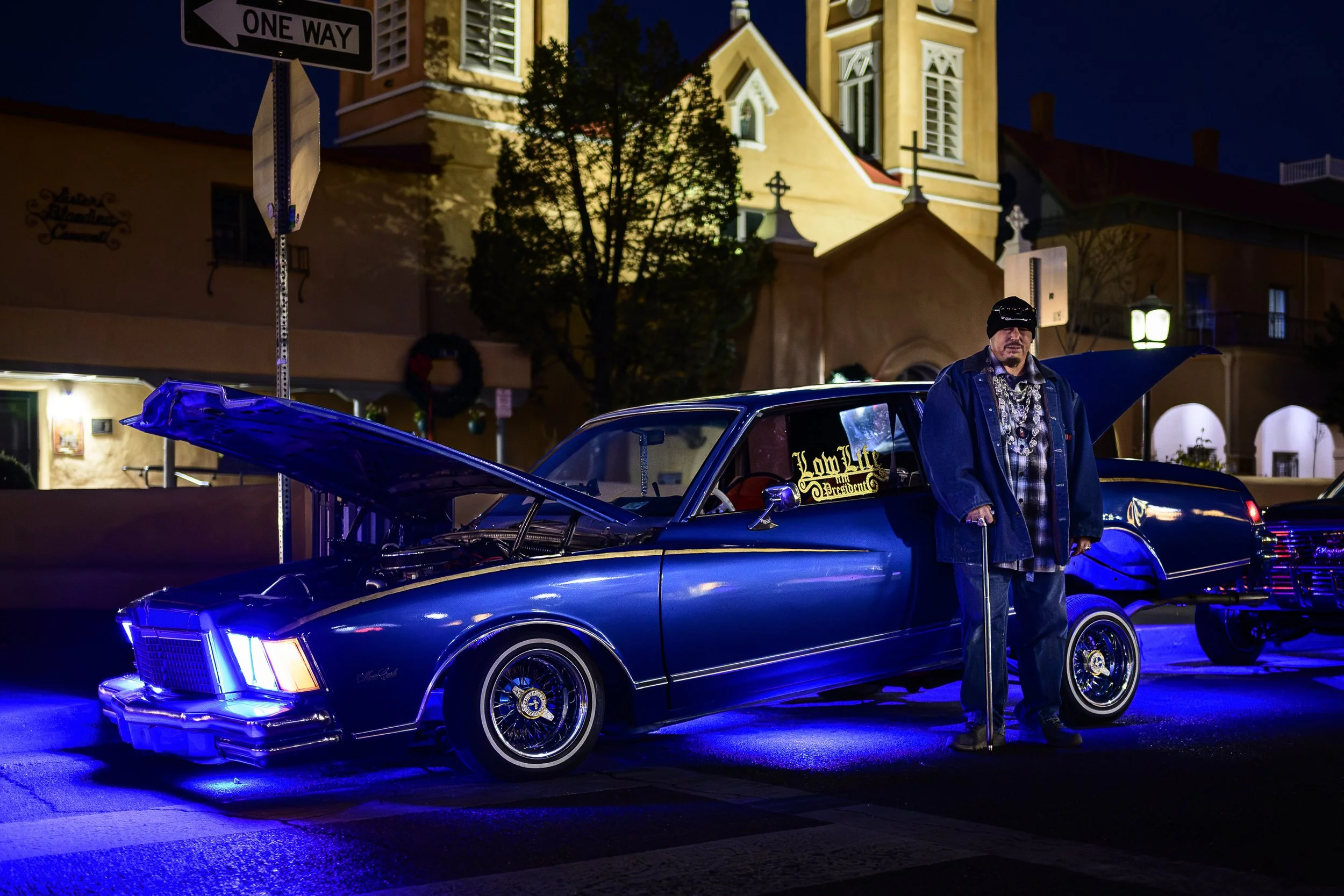 A man standing in front of his chevorlet monte carlo lowrider, in front of San Felipe de Neri Parish | Albuquerque, NM
