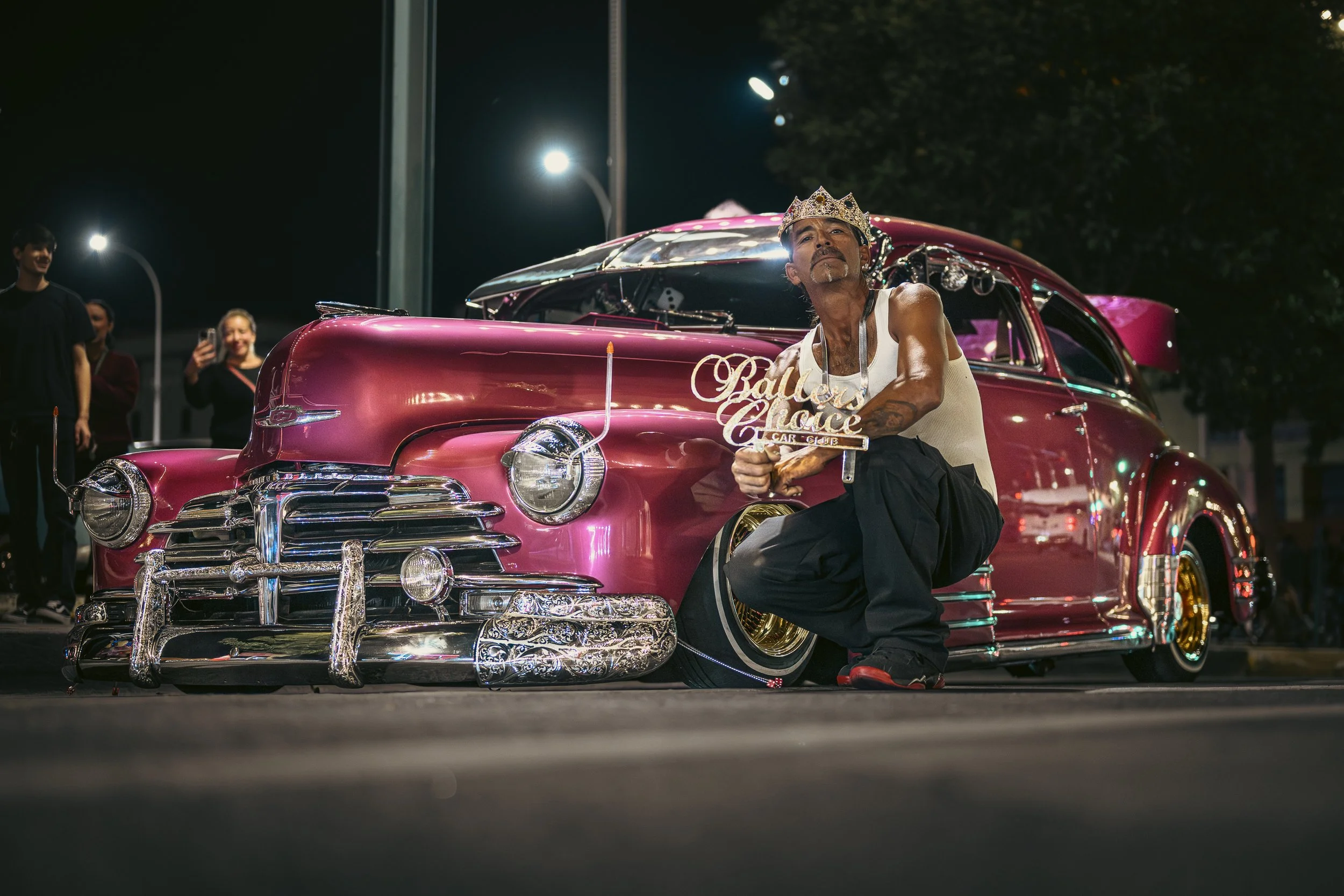 Man posing beside a pink classic lowrider at night in New Mexico.