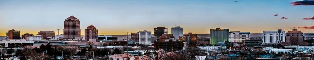 City skyline at sunset with various high-rise buildings and colorful sky.