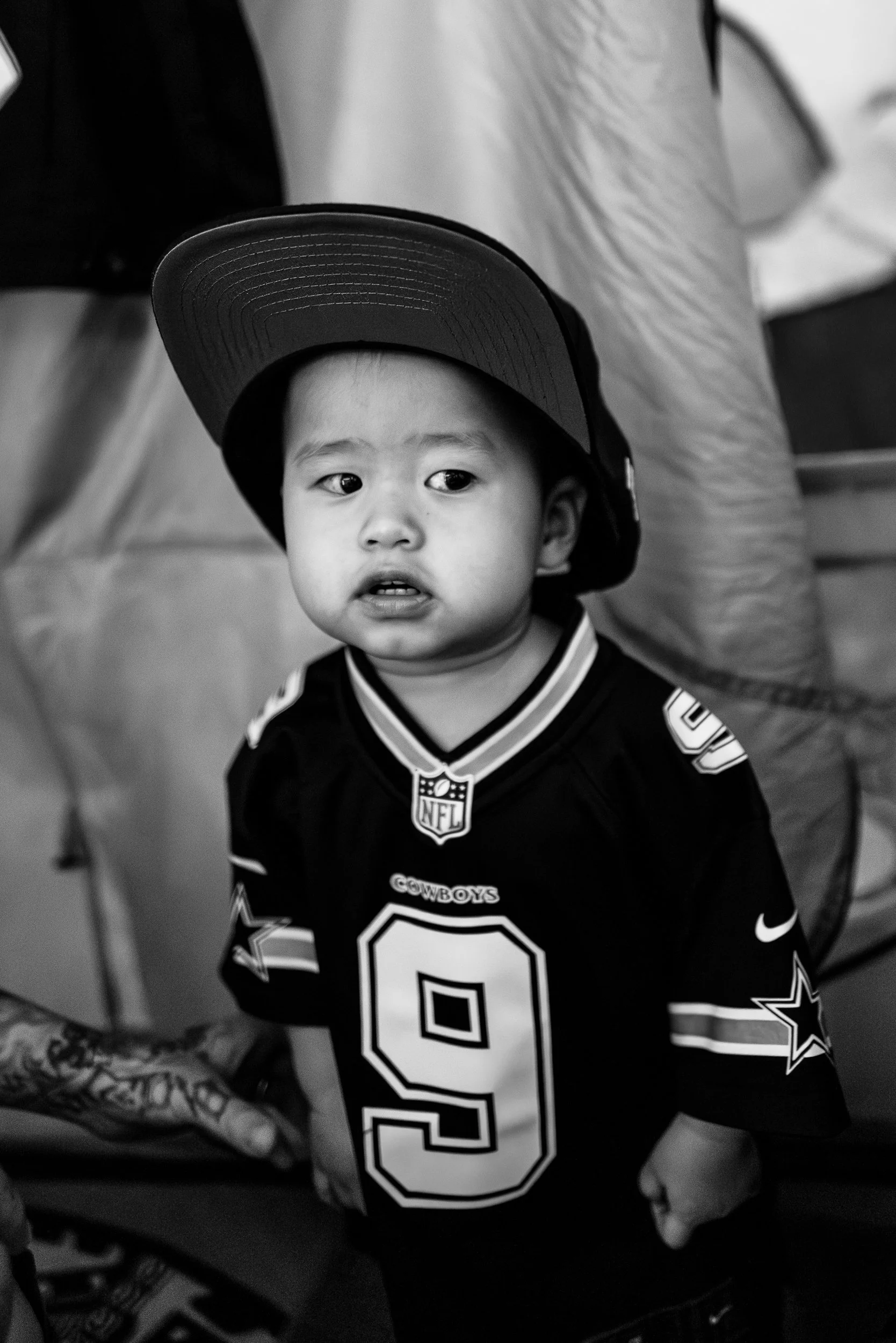 A young boy wearing a football jersey and a cap, looking to the side, black and white photo.