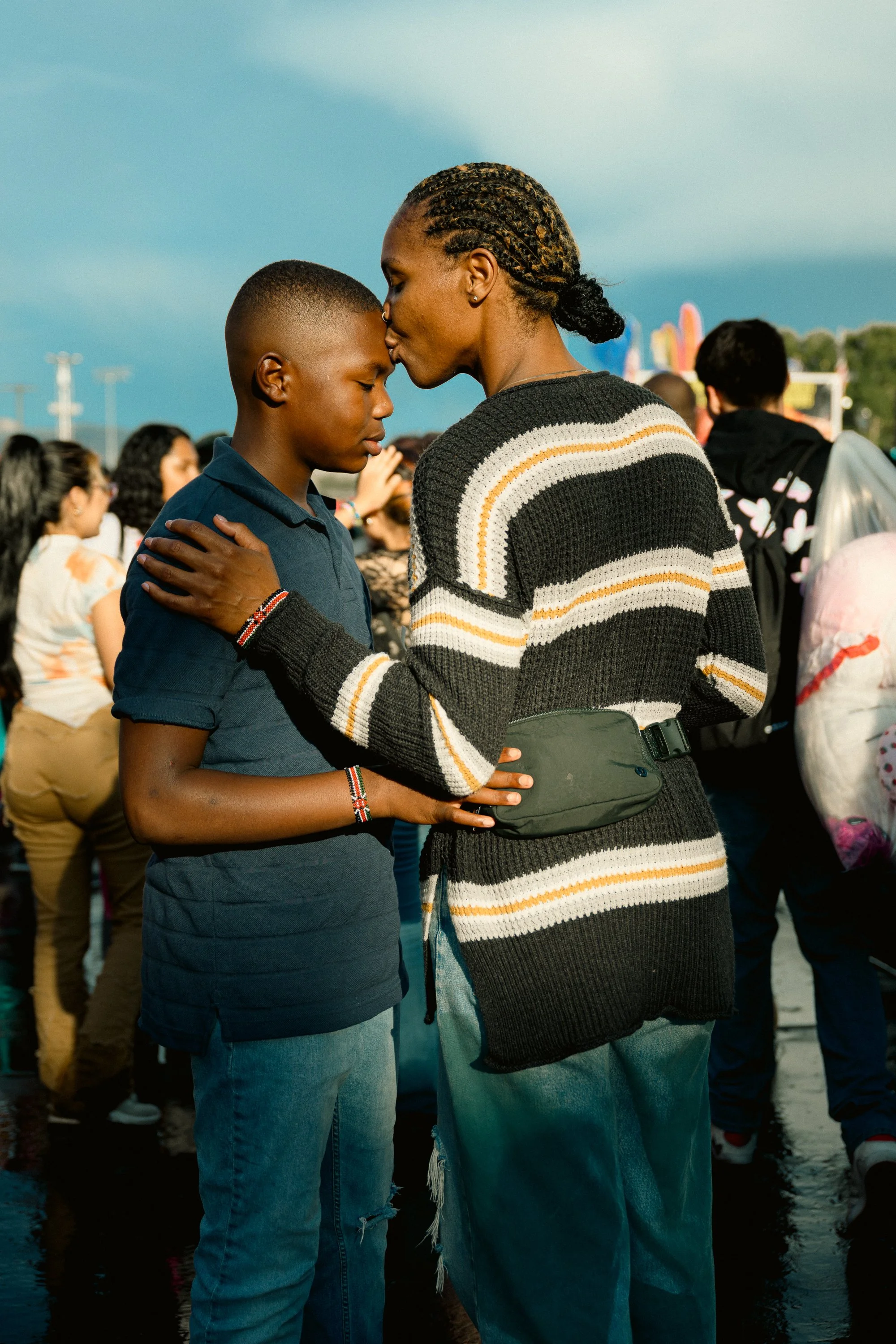 A woman and a boy share a tender moment with their foreheads touching and eyes closed at an outdoor gathering.