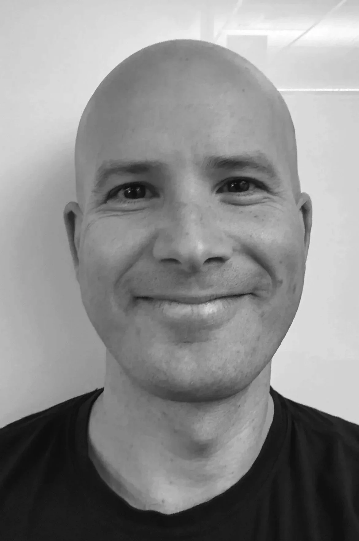 Close-up portrait of a bald man with a beard, smiling and wearing a dark shirt.