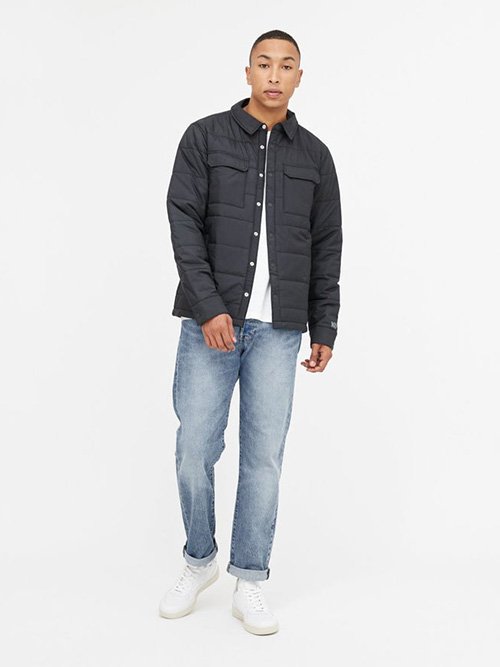 Eco-Friendly Clothing Brands: tentree model wears light wash denim, white shoes, and a dark blue quilted jacket over a white t-shirt.