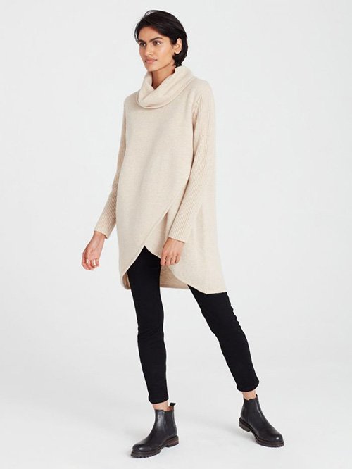 Eco-Friendly Clothing Brands: Model wears Thought Clothing's cowl-neck sweater dress with an overlapping hem above the knee. The dress is paired with blank pants and black boots.