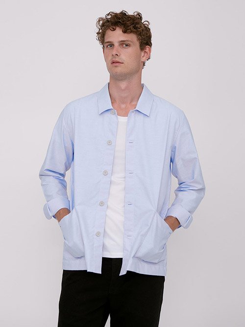 Eco-Friendly Clothing Brands: Model wears Organic Basics' light blue button-down on top of a white t-shirt, paired with blank pants.