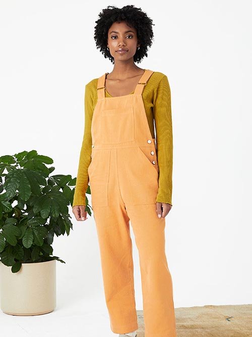 Eco-Friendly Clothing Brands: Model wears Back Beat Co's mustard long-sleeve v-neck shirt with bright orange overalls on top.