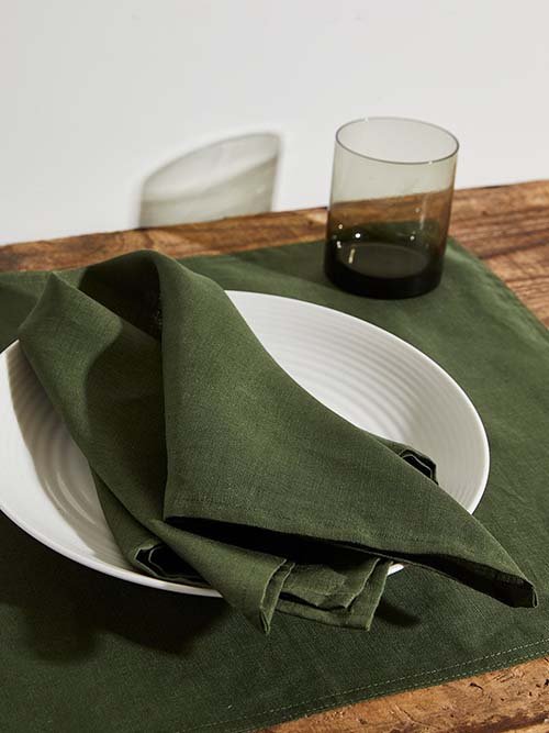 Cloth Napkins: Bed Threads' sage green linen napkins lay on a white plate, matching sage placemat, and near a transparent sage class.