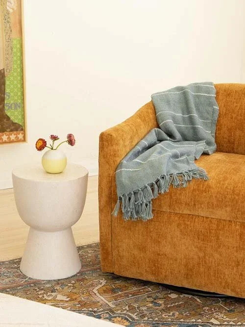 eco-friendly furniture - joybird - orange gold velvet swivel chair with a throw blanket next to a neutral accent table