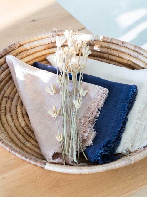 Cloth Napkins: NOMA Collective's fringe linen napkins lay in a basket with plants on top.