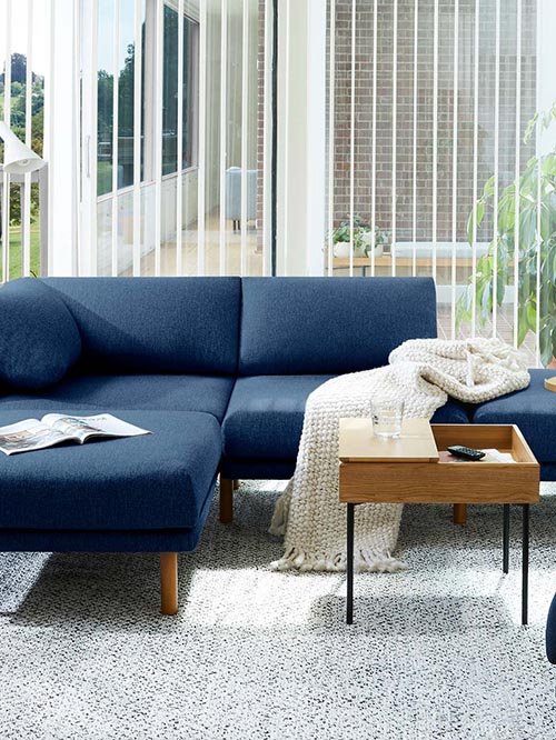 eco-friendly furniture - burrow - dark blue sectional couch with brown legs in a living room with a white throw pillow and a walnut brown coffee table