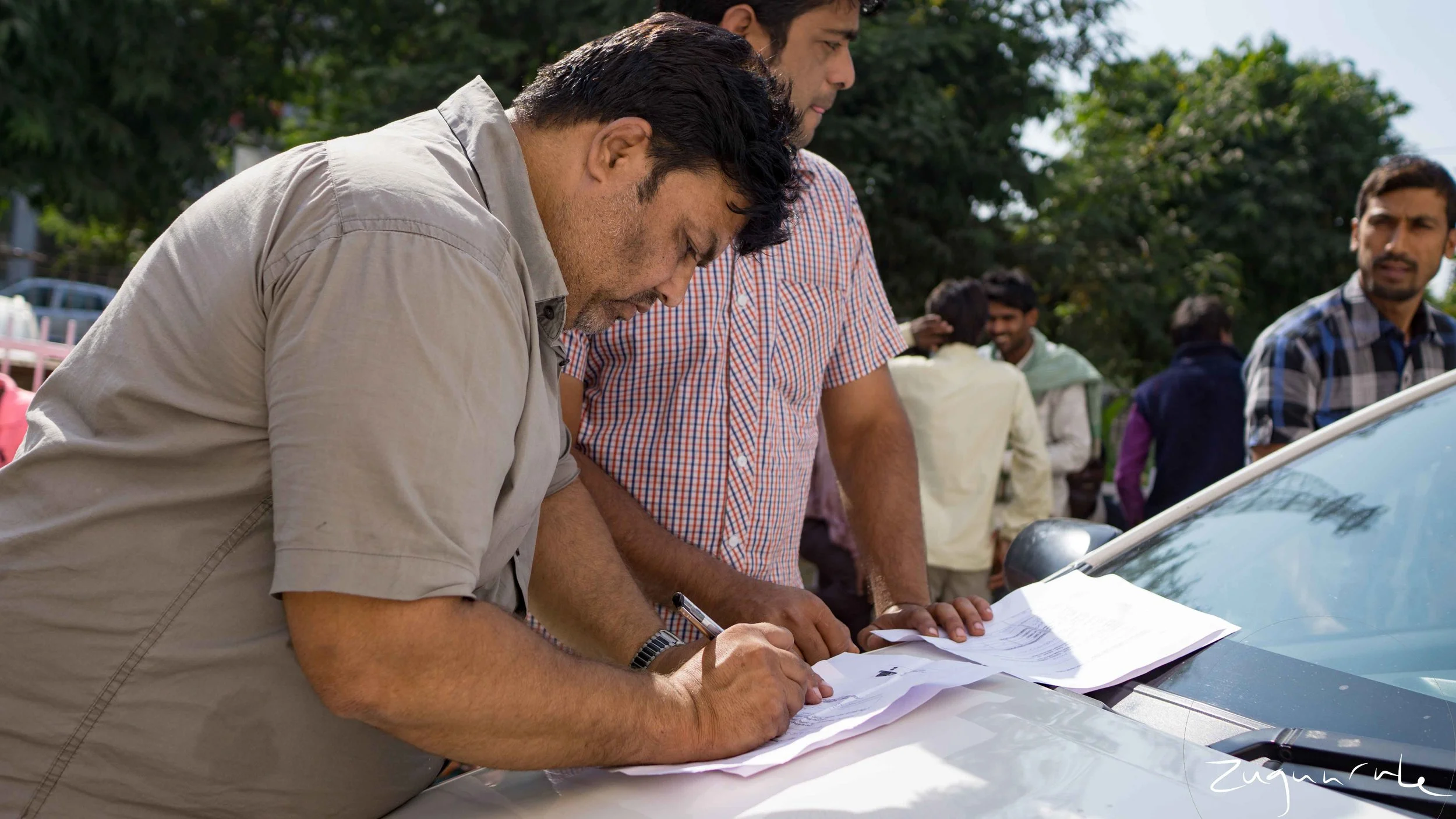 A man fills out exchange paperwork on the hood of a car (Jaipur)