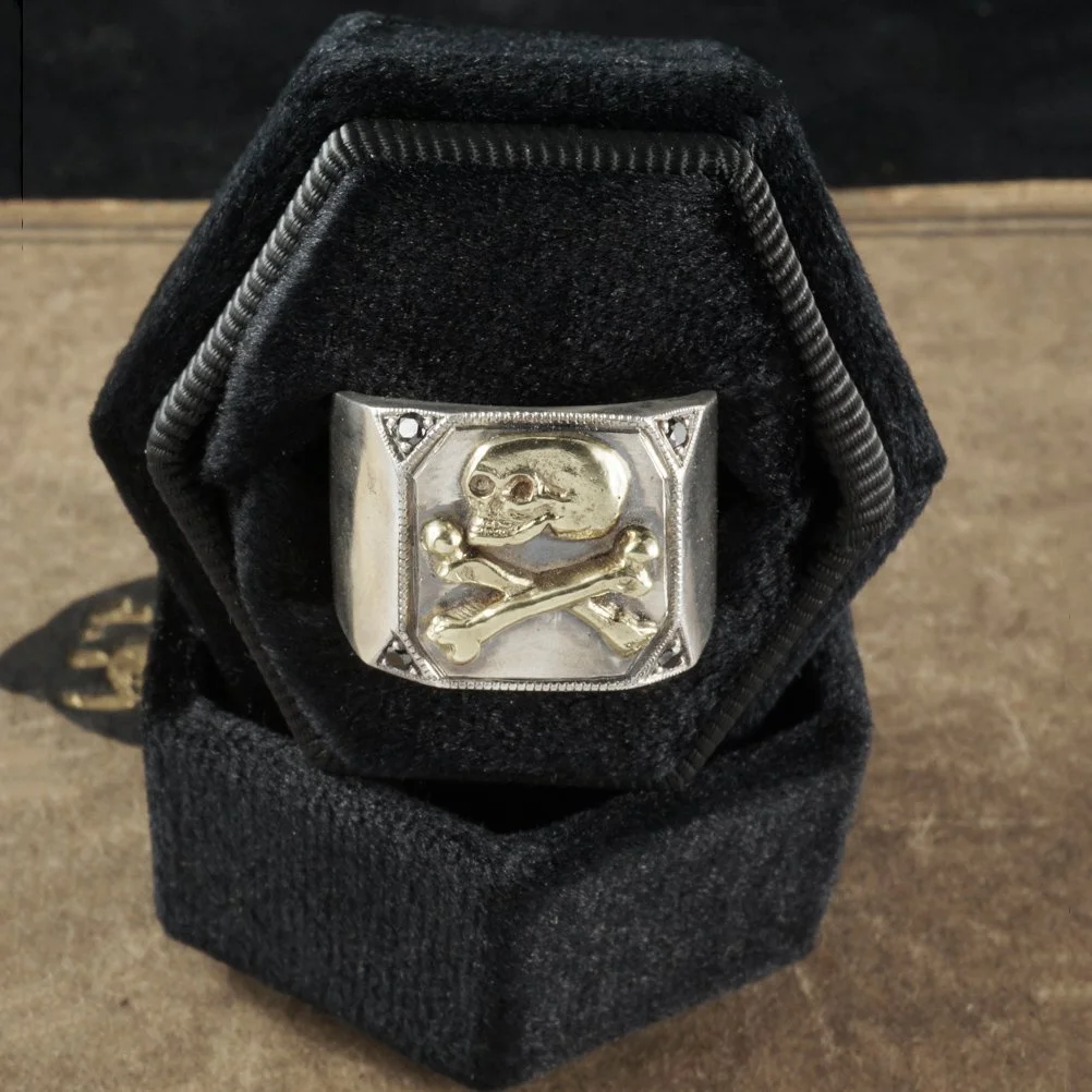 This image is of a gold and silver skull signet ring with black diamonds in a black ring box.