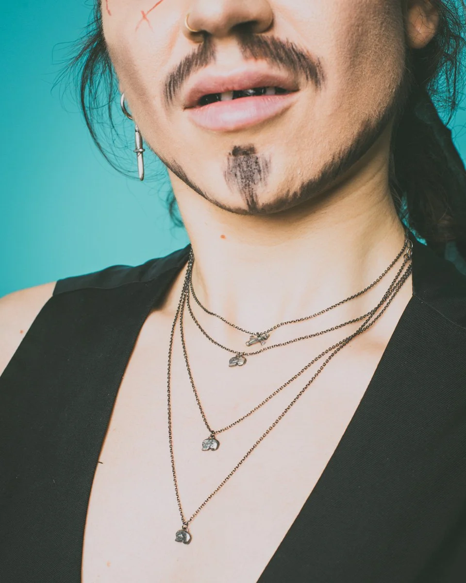 This image is of small silver and gold skull and crossbones pendants being worn on a drag king pirate