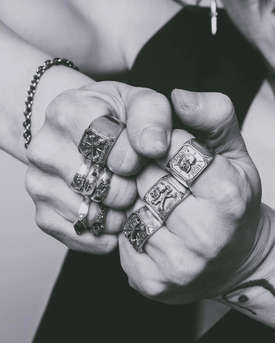 This image is of a hand wearing multiple Memento mori themed silver skull rings