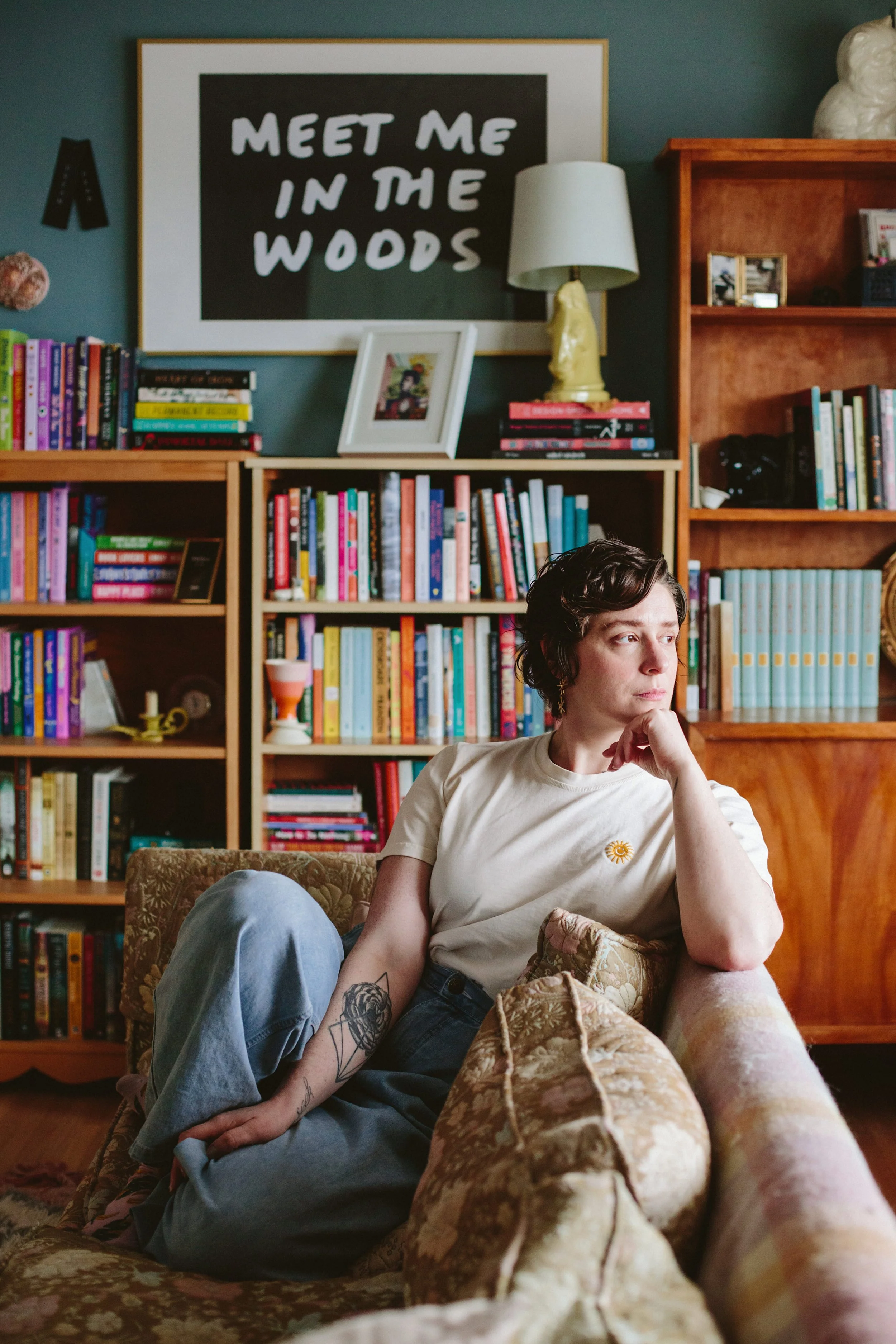 Elyse Bouvier, a white woman with short wavy hair, sits on a couch looking out a window with bookshelves behind her.