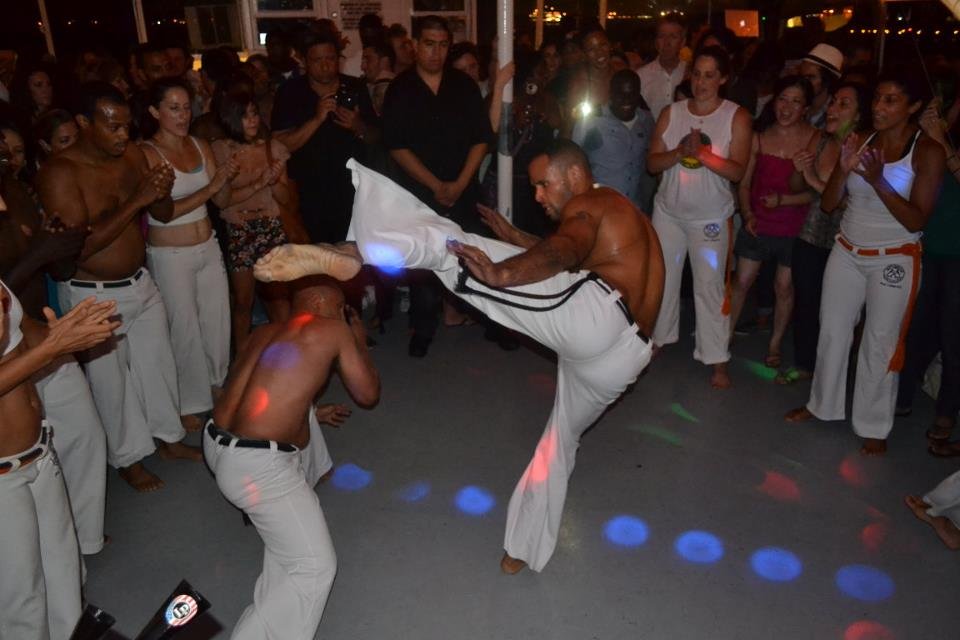 A Capoeira game unfolds in a circle as musicians and community members watch.
