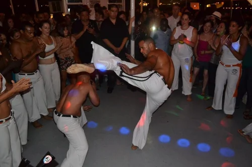 A Capoeira game unfolds in a circle as musicians and community members watch.