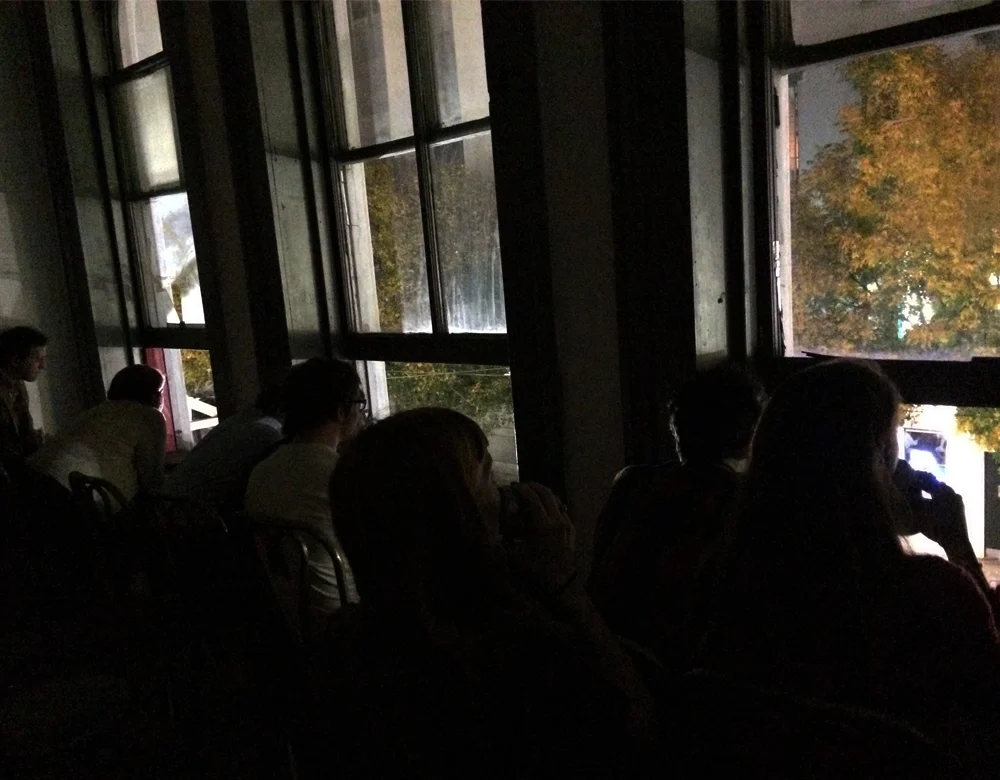 The audience watches from a second story window across the street