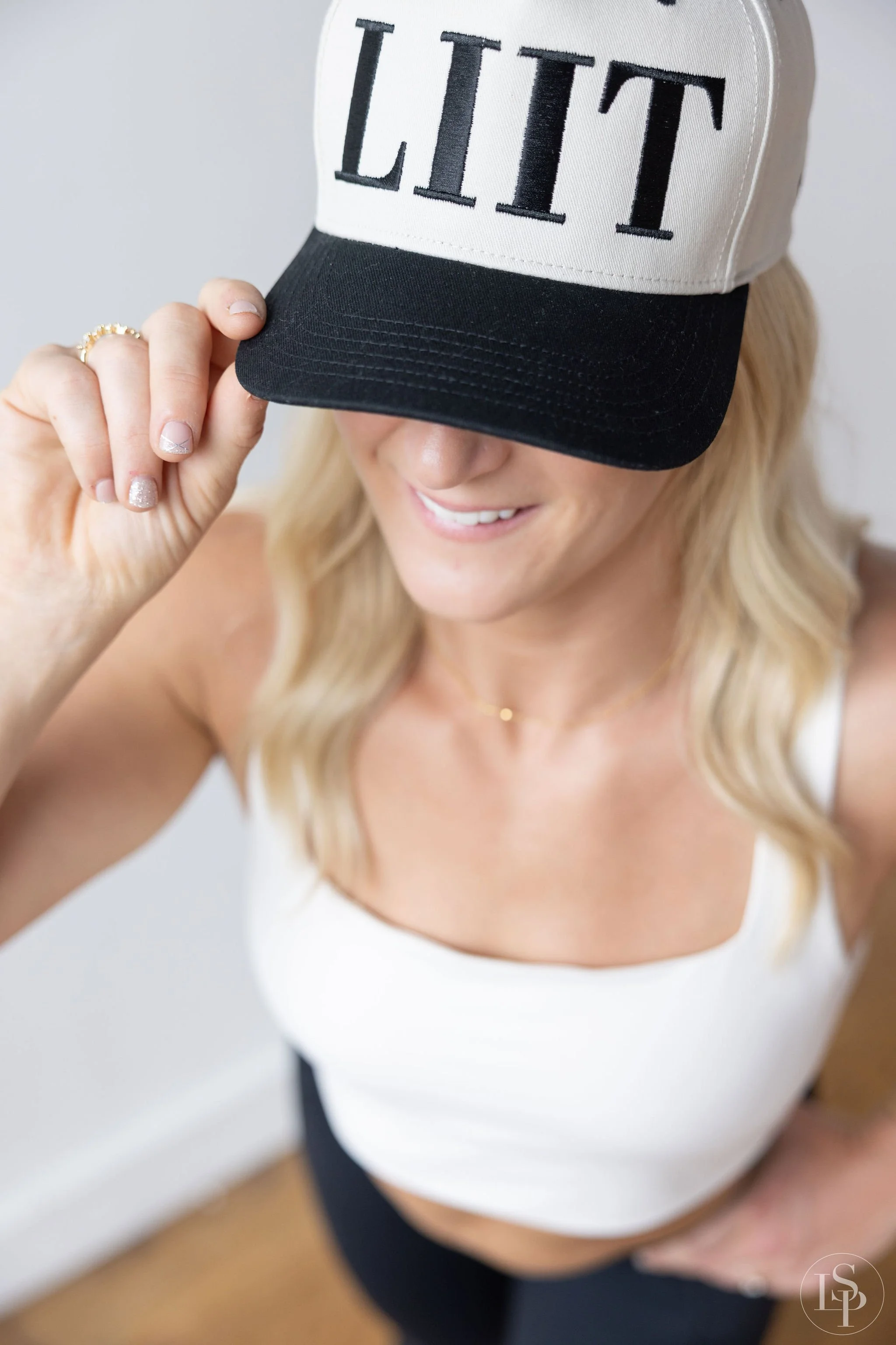 A woman is adjusting a black and white trucker hat with the word 'LIT' embroidered on the front panel. Commercial brand photography near me. Cleveland.